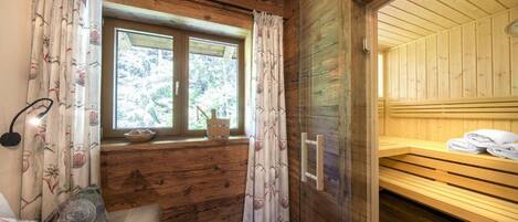A wooden cabin room with a window, a bench, and a sauna area.