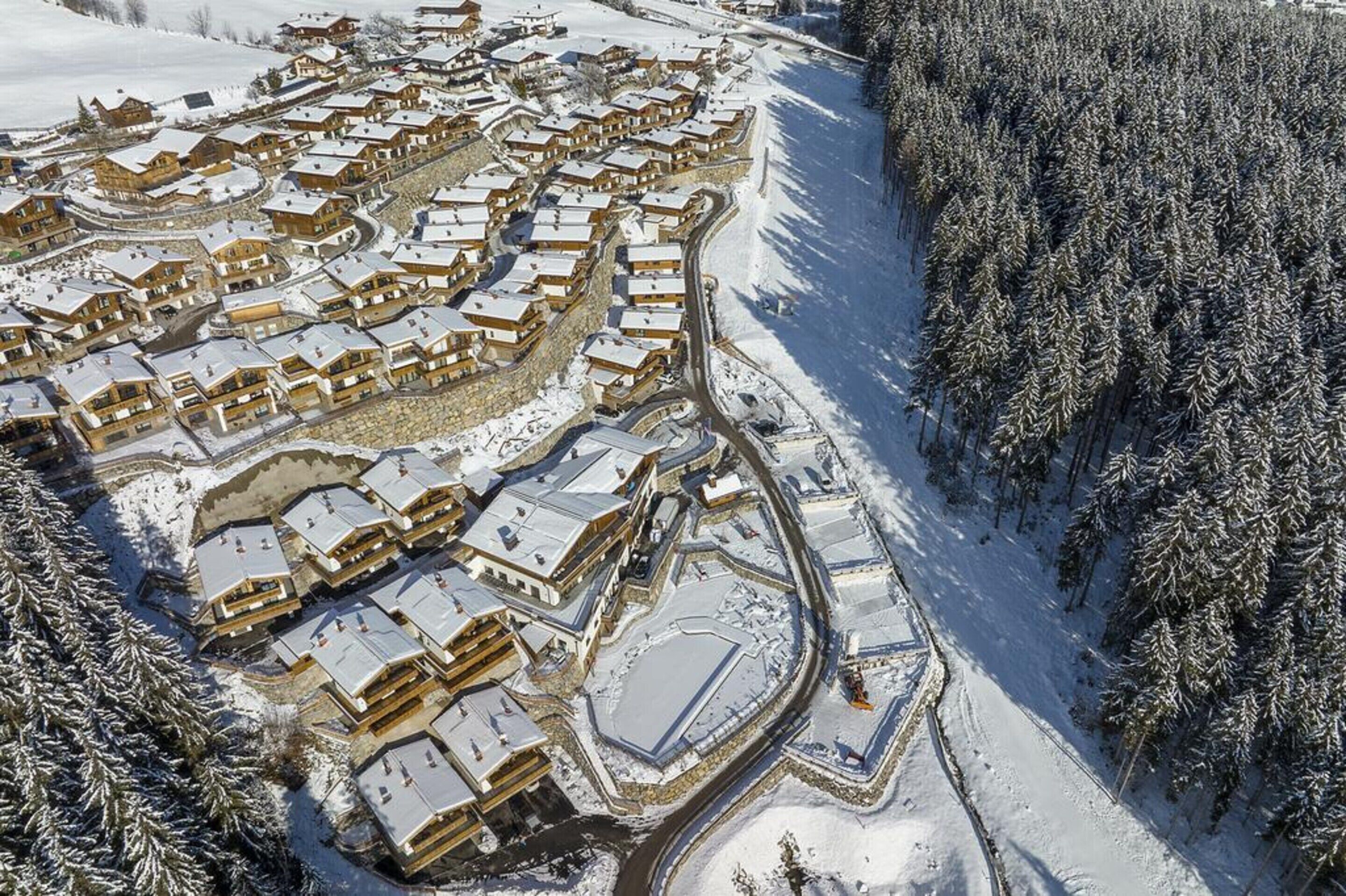 Ett flygbildsbild av ett snötäckt semesterområde med flera byggnader i chaletstil, placerade i en halvcirkelformad formation och omgivna av tät skog.