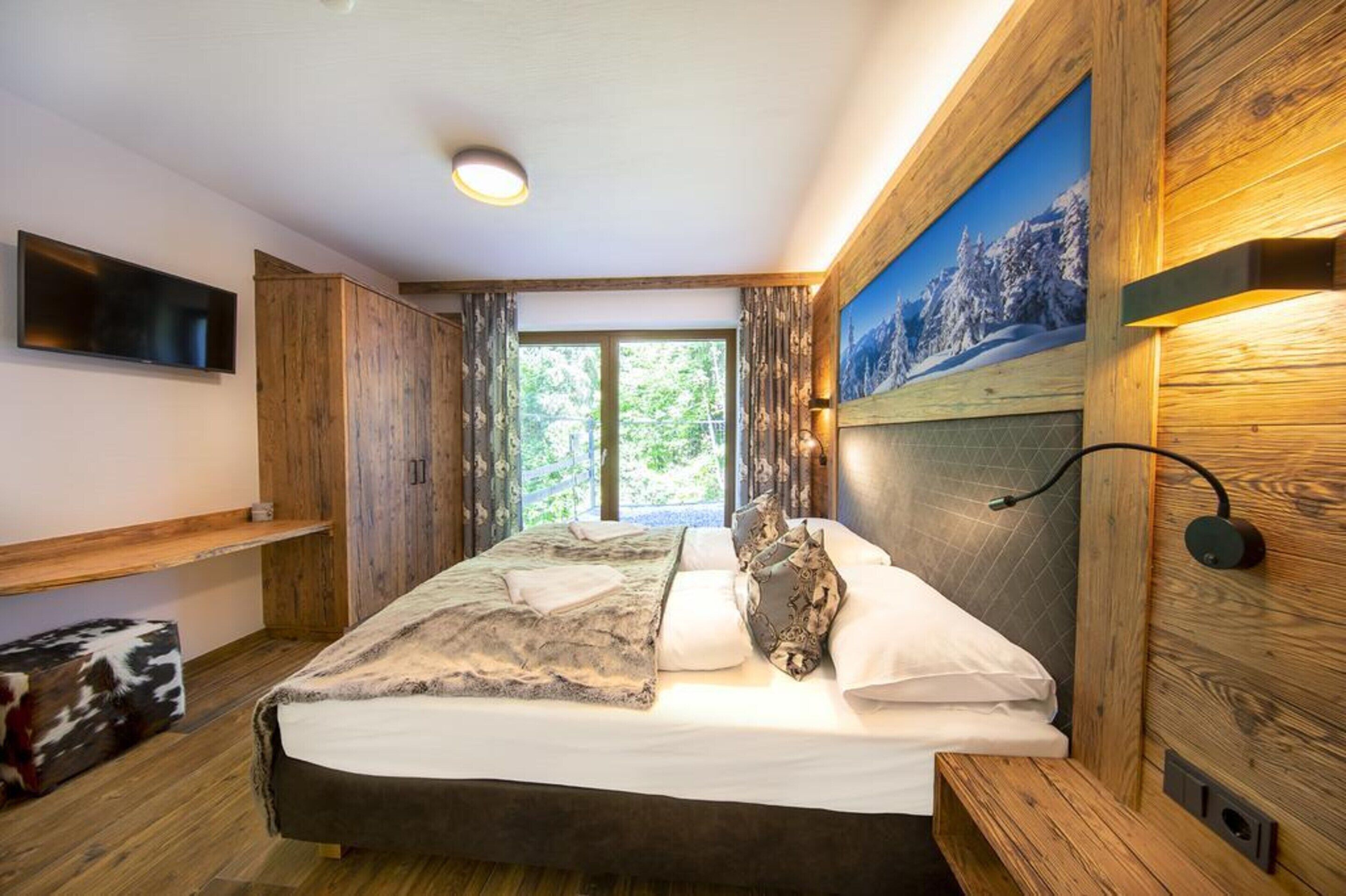 A bedroom with a bed, wooden walls, a painting, and a TV on the wall.