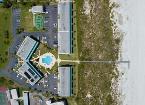 An aerial view of a coastal hotel with a parking lot, a swimming pool, and a beach.