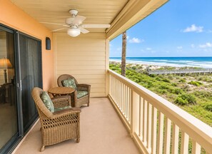 A balcony with wicker furniture, a ceiling fan, and a view of the beach.