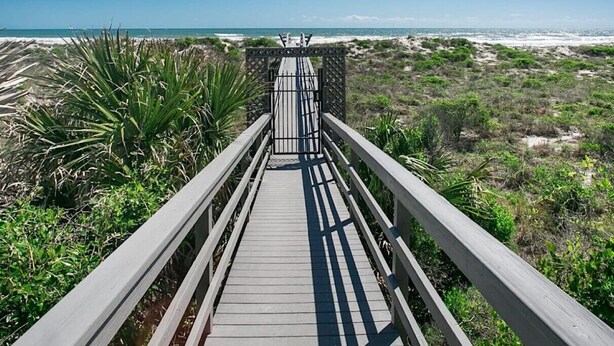 A wooden boardwalk leading to a beach with a clear sky.