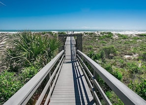 A wooden boardwalk leading to a beach with a clear sky.