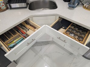 Una cucina con un piano di lavoro bianco, un lavello in acciaio inossidabile e un divisorio per cassetti con utensili e spezie.