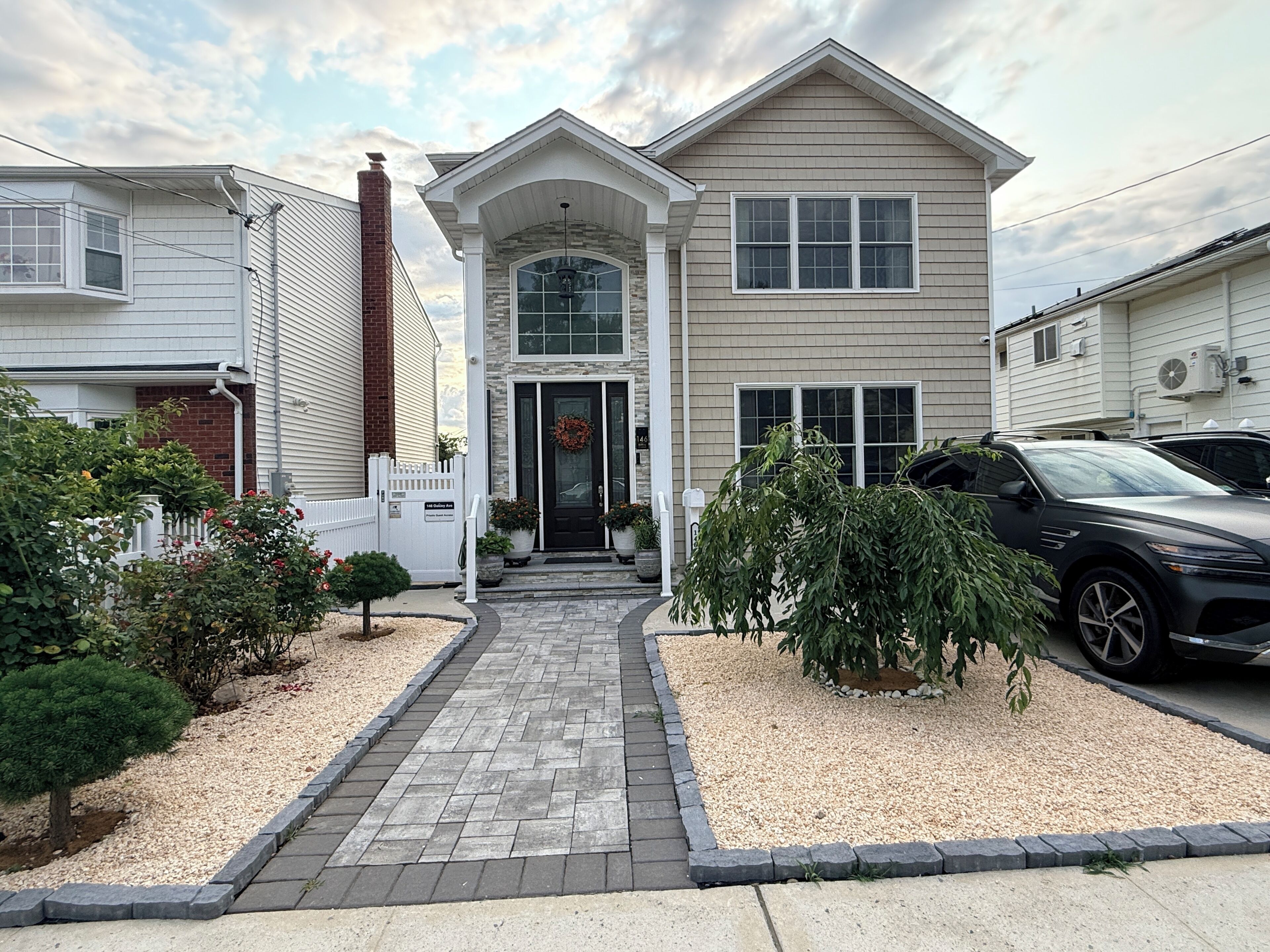 A two-story house with a front porch, a driveway, and a car parked in the driveway.