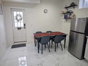 Una cocina compacta con una mesa de comedor, sillas, un refrigerador y un reloj en la pared.