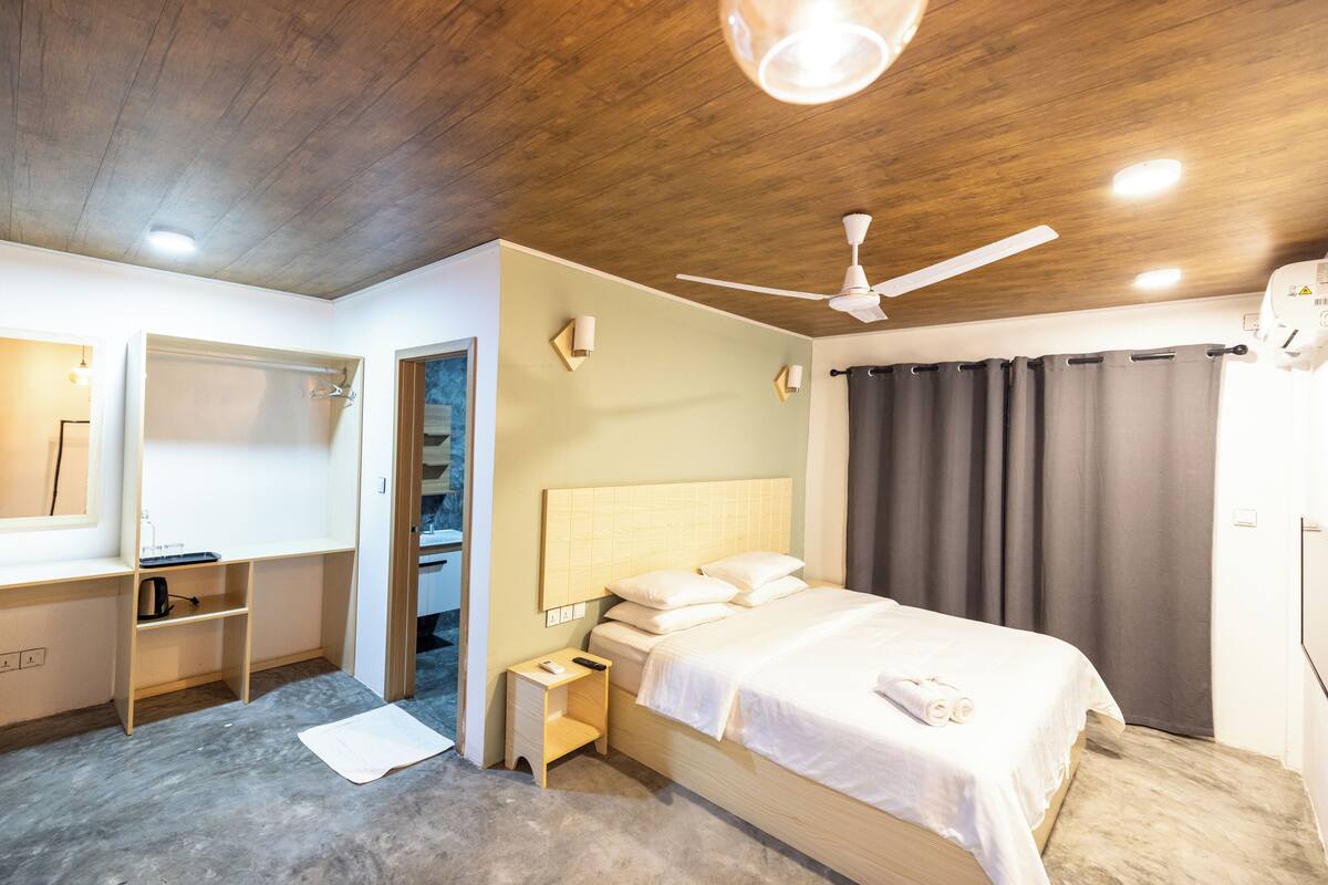 Une chambre à coucher comprenant un lit, une table de chevet, une commode, un ventilateur de plafond et une armoire.