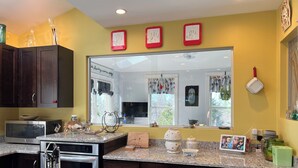 A modern kitchen with dark wooden cabinets, a granite countertop, a microwave, a stove, and a dishwasher. There are decorative items and a large mirror above the sink.
