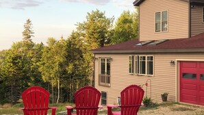 A house with a red garage door, a small attached garage, and a covered porch area with three red Adirondack chairs.