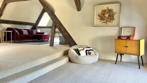 Une chambre à coucher de style loft avec un plafond en pente, un canapé rouge, un fauteuil en forme de poire blanc, une armoire en bois et une œuvre d’art encadrée accrochée au mur.