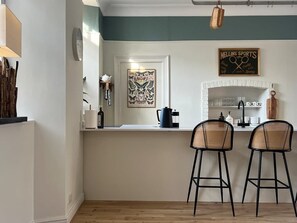 A kitchen with a white island, two bar stools, a coffee maker, and a framed butterfly artwork.