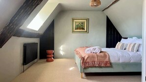 Une chambre avec un plafond en pente, un radiateur, un lit avec des oreillers, un tableau encadré au mur et un luminaire suspendu.