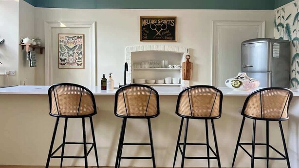 Une cuisine équipée de trois tabourets de bar, d’un réfrigérateur et d’un panneau d’affichage noir.