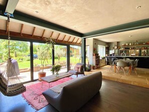 A spacious living room with a large sofa, a hanging chair, and a dining area with a table and chairs. - Spacious Family Home - Central Frome (Frome)