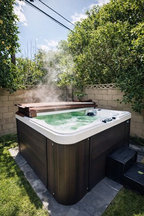 Un jacuzzi con plataforma de madera, rodeado por un muro de ladrillo y follaje.