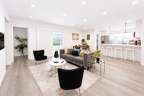 A modern living room with a sofa, two black chairs, a coffee table, and a kitchen area with a bar counter.