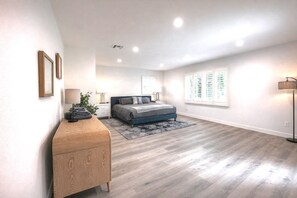Un dormitorio con cama, mesitas de noche, cómoda, lámpara y ventana con persianas.