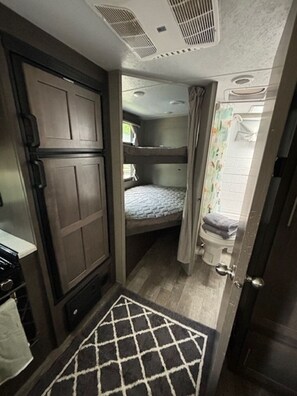 A compact RV interior with a bunk bed, a small kitchenette, and a shower area. - Luxury Meets Adventure. Glamp in Style. (Roscommon)