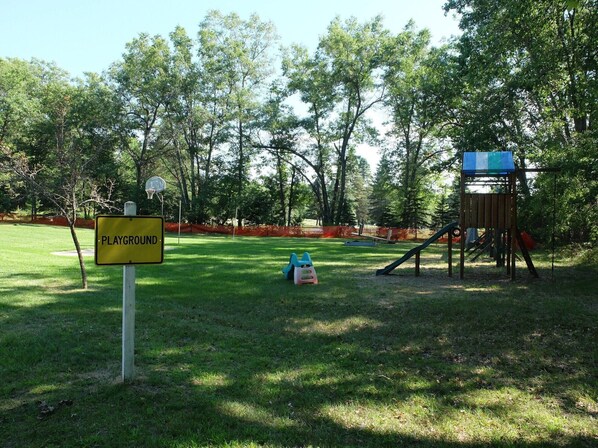 A playground area with a yellow sign, a slide, and a climbing structure. - Luxury Meets Adventure. Glamp in Style. (Roscommon)