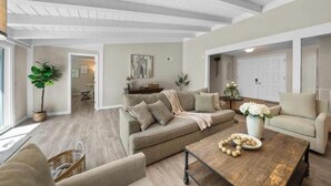 A spacious living room with a high ceiling, a large sofa, a coffee table with decorative items, and a view of the adjacent dining area. - Hidden Paradise｜ BBQ & Fish Pond (Glendora)