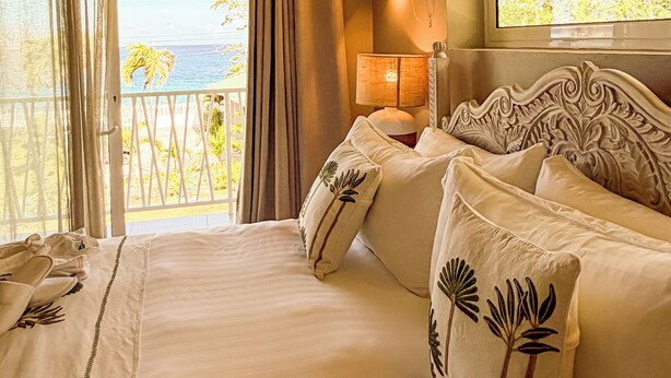 Une chambre d’hôtel avec un balcon, un lit avec des oreillers, une lampe et une vue sur la mer.