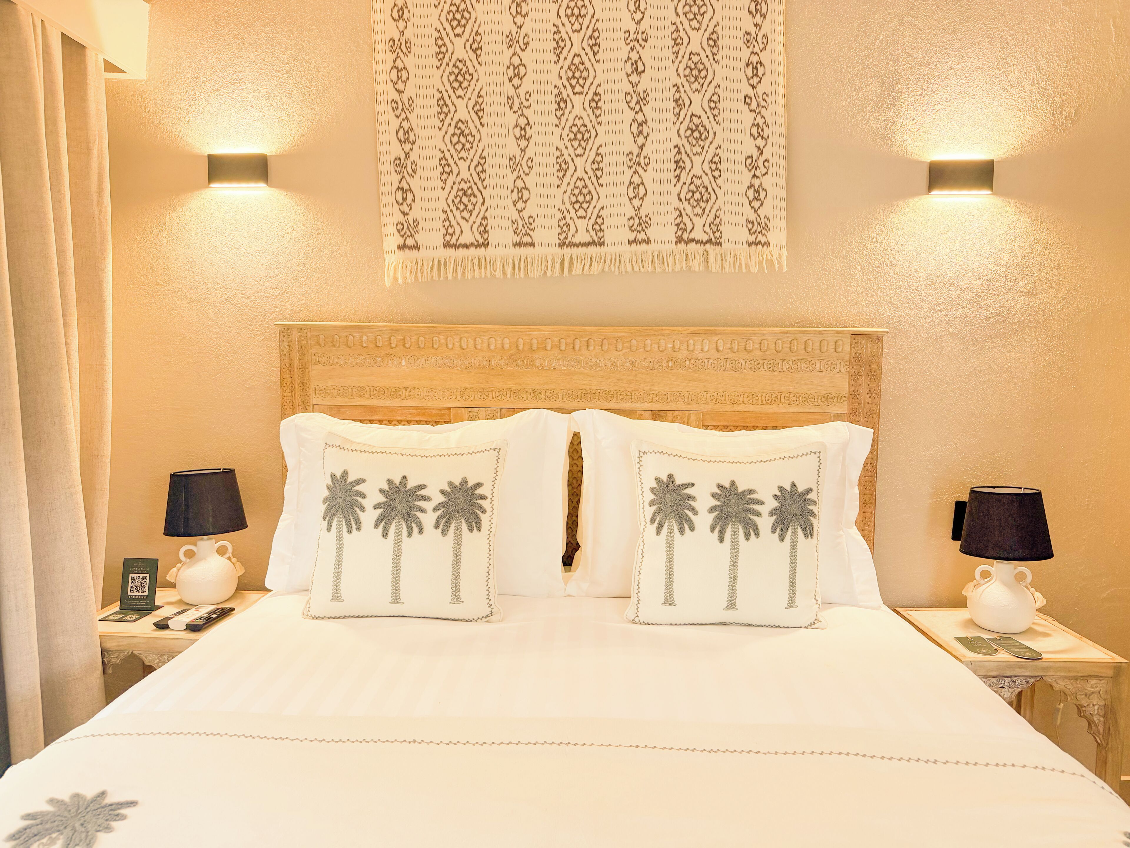 Habitación de hotel con cama, dos mesitas de noche, un adorno en la pared y un cabecero con tallas detalladas.
