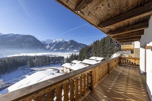 A wooden balcony with a view of snow-covered mountains and a forest.