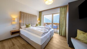 Habitación de hotel con cama, lámparas de noche, televisor y balcón con vistas.