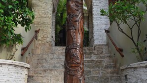 A stone staircase with a central wooden pillar featuring carvings, surrounded by lush greenery and a white building with an arched entrance. - 2BR Kobah • 1 Block to Beach & 5th - Pool+Gym (Playa del Carmen)
