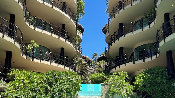 A multi-story hotel with a central pool, balconies with plants, and a waterfall feature. - 2BR Kobah • 1 Block to Beach & 5th - Pool+Gym (Playa del Carmen)