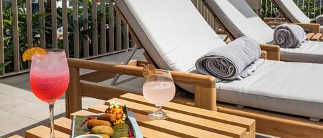 Un espace de détente aménagé sur le toit, avec des fauteuils en bois, une table où sont servis des boissons et des en-cas, et une vue sur les palmiers et les montagnes.
