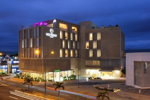A modern hotel with a prominent 'Orquesta' sign, featuring a mix of glass and concrete architecture, and a 'Monte' restaurant at the ground level.