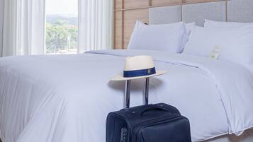 Une chambre d’hôtel avec un grand lit, du linge de lit blanc, une tête de lit en bois, une valise et un chapeau posés sur une petite table.