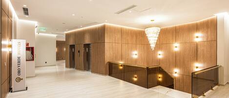 Vestíbulo de hotel con paneles de madera, un candelabro y un letrero que indica HOTEL ORO VERDE.