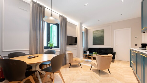 A modern living room with a dining area, a flat-screen TV mounted on the wall, and a kitchen with blue cabinets. - STAYMADRID - Bernabeu Luxe Apartment (Madrid)