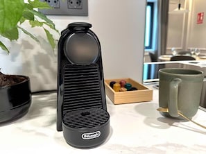 A DeLonghi electric kettle on a kitchen counter with a potted plant, a wooden box with colorful items, and a ceramic mug.