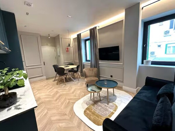 Una sala de estar moderna con sofá, una mesa de centro, un comedor con sillas y un televisor montado en la pared.