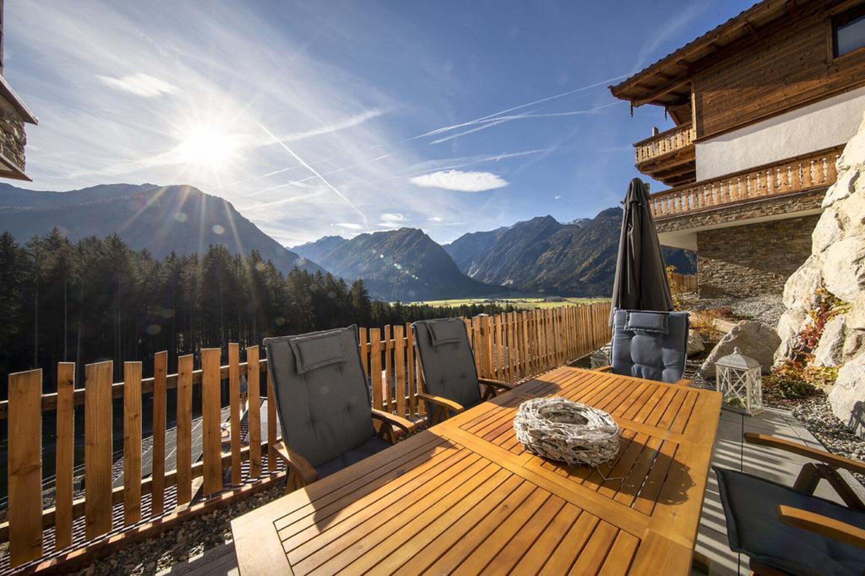 Une table en bois, entourée de chaises, avec une corde posée dessus, donnant sur un paysage montagneux agrémenté d’une clôture en bois et d’un mur de pierres.