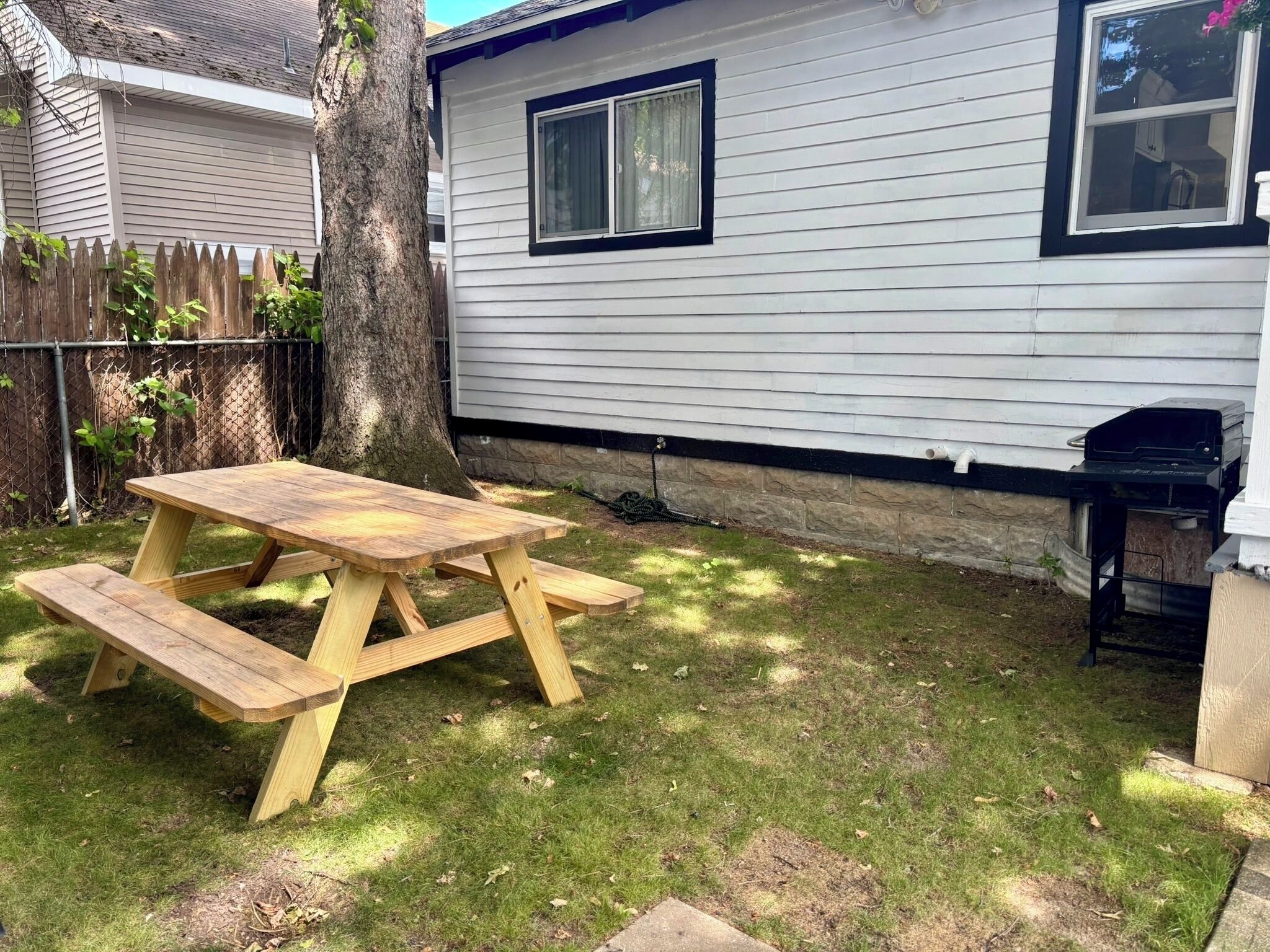 Una mesa de picnic de madera en un patio trasero, con una casa al fondo.