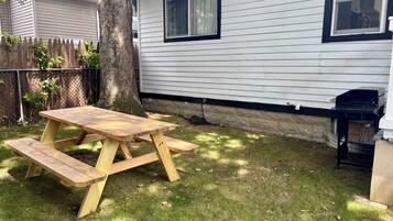 Una mesa de picnic de madera en un patio trasero, con una casa al fondo.