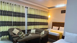 Une chambre d’hôtel avec un lit, deux canapés, une table basse et des rideaux à motifs.