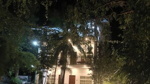 Un bâtiment à deux étages doté d’un balcon, entouré d’arbres et illuminé par des guirlandes lumineuses.