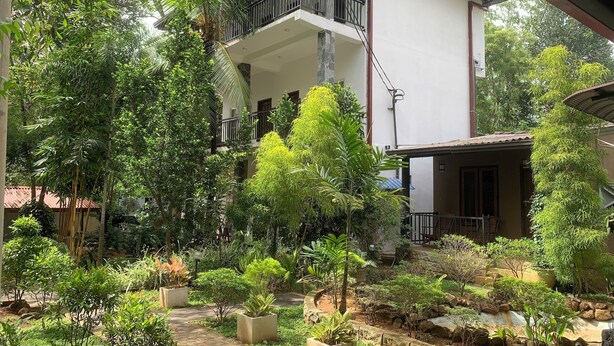 Une cour intérieure agrémentée de plantes en pot, un chemin bordé de briques et un bâtiment à deux étages doté de balcons.