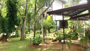 Un jardin agrémenté de plantes en pot, une pergola et un bâtiment doté d’un toit rouge.