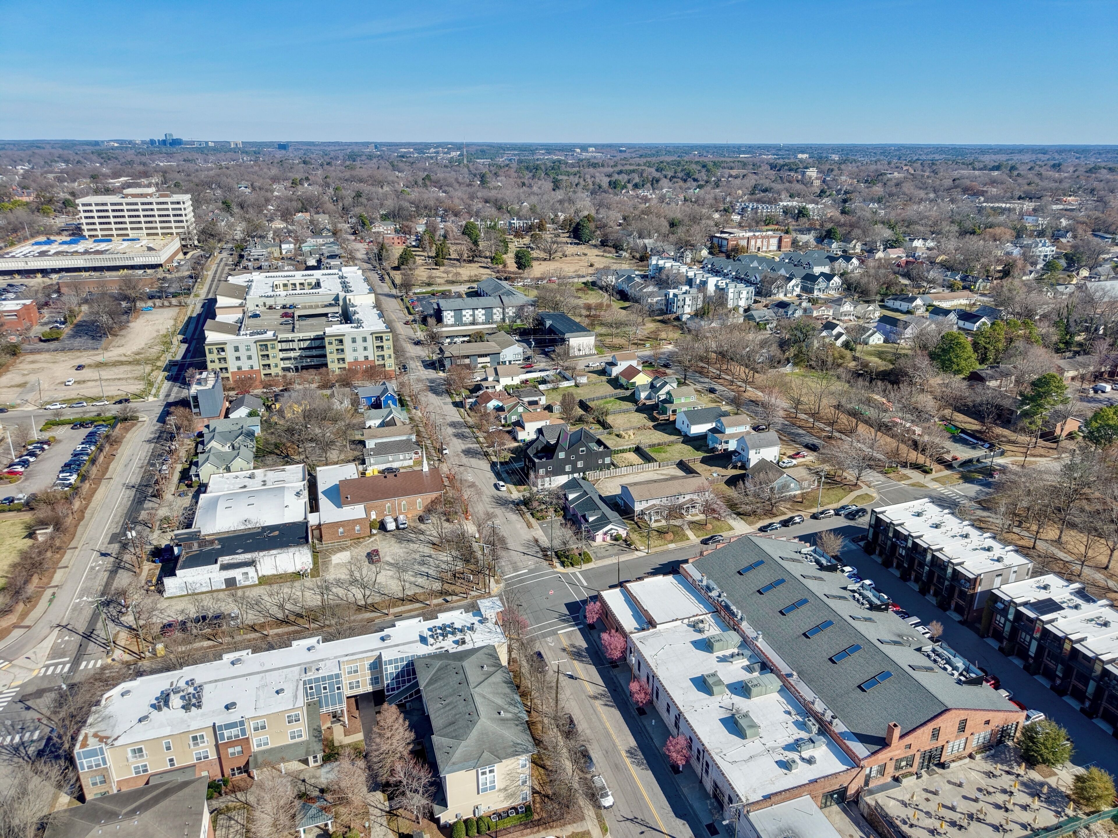Vista aérea de una zona residencial con varios edificios, carreteras y un horizonte urbano lejano.