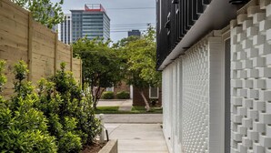 A narrow concrete pathway flanked by a wooden fence and a white brick wall with a geometric pattern. - Mini Metro - Downtown Rooftop with Skyline View! (Raleigh)