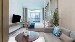 A modern hotel room with a large bed, a television, a sofa, and a view of the cityscape. - Luxury Canal-View Studio (Business Bay)