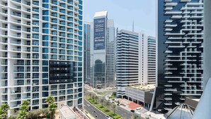 A modern high-rise hotel with a prominent digital bank advertisement, a pool area, and a well-maintained urban street view. - Luxury Canal-View Studio (Business Bay)