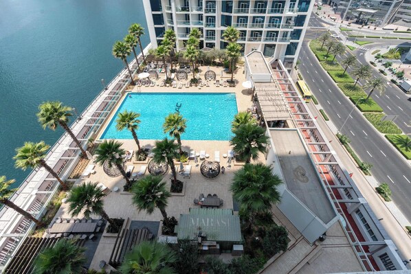 A rooftop pool with palm trees, a lounge area, and a view of the city.