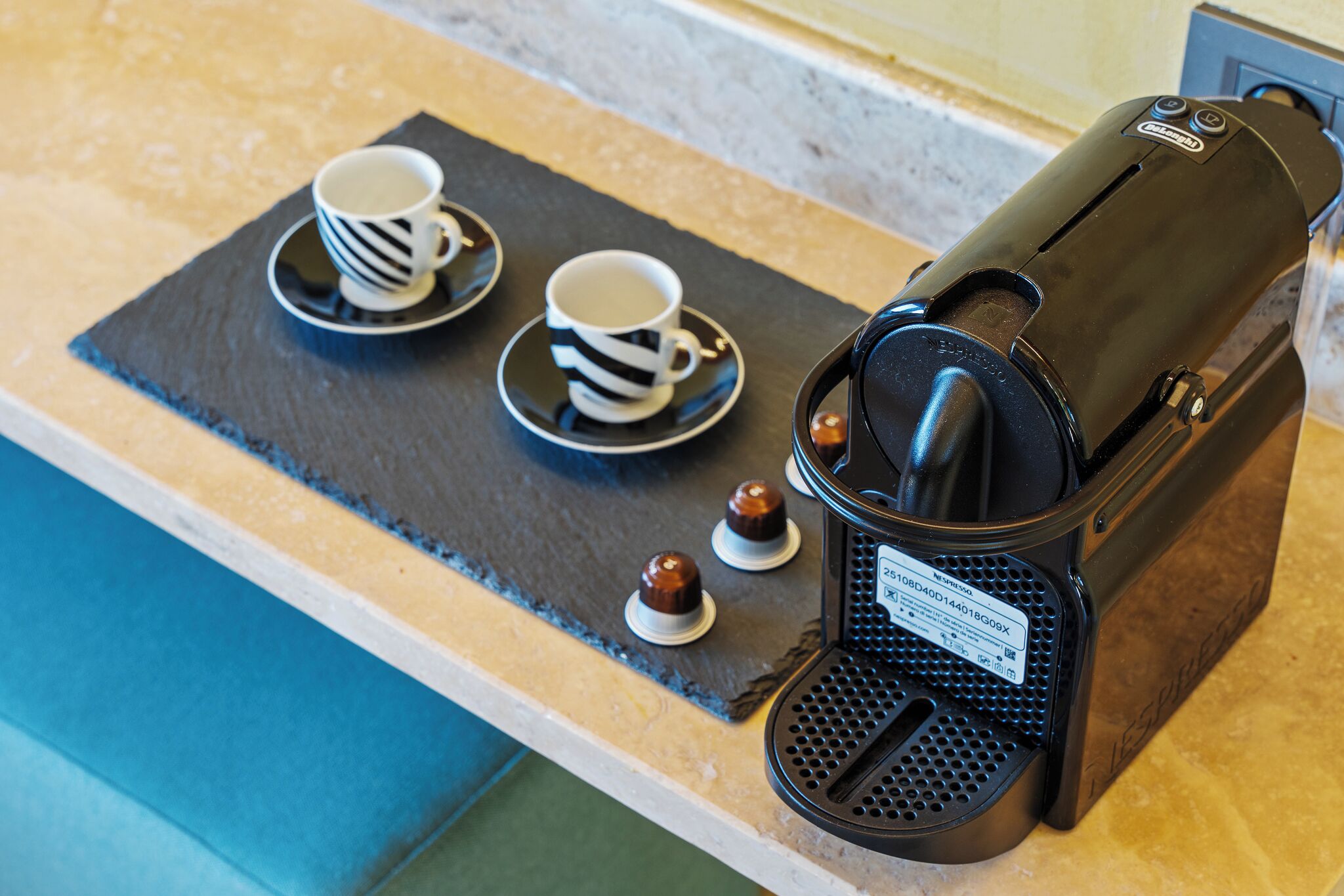 A coffee machine with a label, two cups with saucers, and two small chocolate-covered items on a tray.